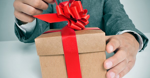 Man opening a corporate gift wrapped in a brown box with a red bow