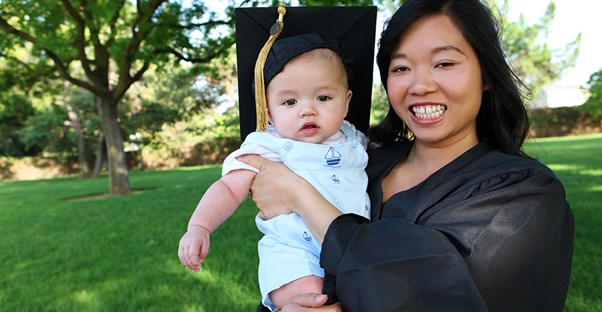 a young single mother wearing a graduation gown holding her infant child who is wearing her graduation cap on her college graduation day