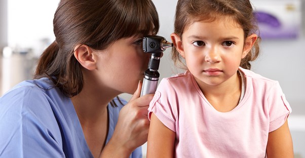 Audiologist looks into the ear of a little girl who looks like she would rather be anywhere else