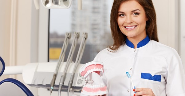 A dental hygienist holds up a toothbrush and a pair of fake teeth
