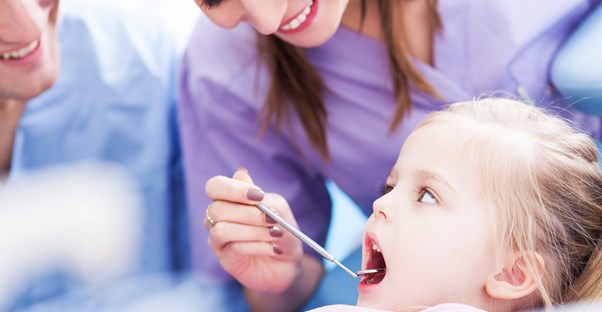 A dental hygienist checks a litle girl's teeth