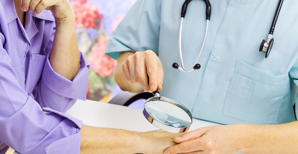 A dermatologist holds a magnifying glass up to examine a hand