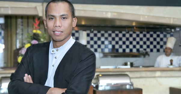 A hospitality manager poses in front of a kitchen