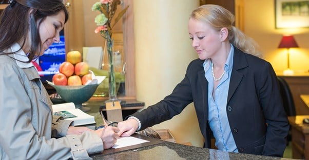 A hospitality manager checks a hotel guest in at the front desk