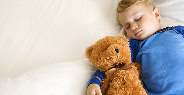 child laying on bed with teddy bear