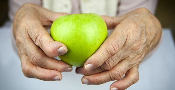 Una mujer mayor sostiene una manzana con sus manos.