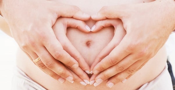 Pregnant belly with hands in a heart. Pregnancy and constipation. 