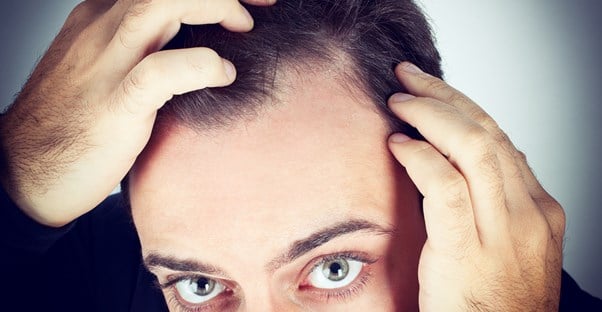 a man examines his side part for hair loss
