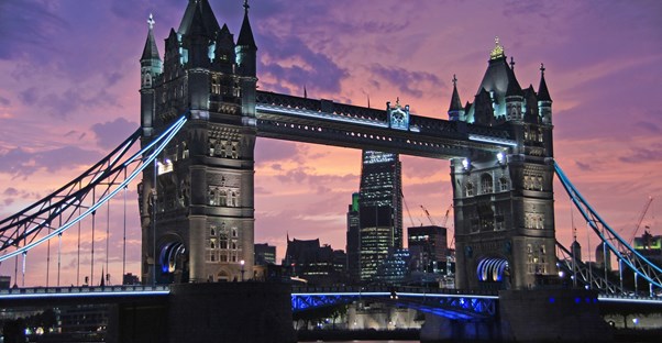 The sun sets behind Tower Bridge in London creating a purple sky.