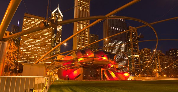 jay pritzker pavilion at night bathed in red light against a backdrop of the chicago skyline