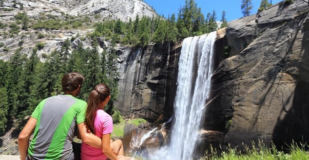 a couple sits enjoying a beautiful waterfall in yosemite national park on their weekend getaway