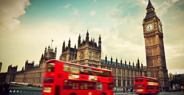 double decker buses travel in front of big ben and the houses of parliament