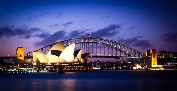 the sydney opera house is lit up at night in front of the sydney harbour bridge