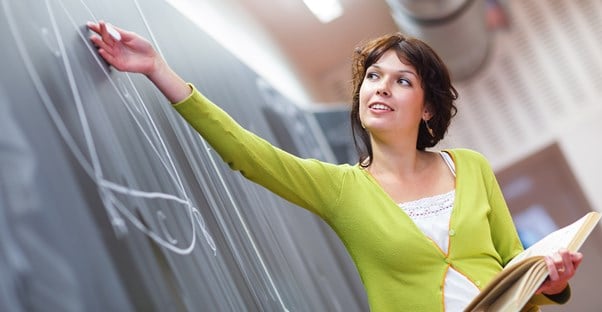 Woman in a booger-colored sweater caresses the chalk board