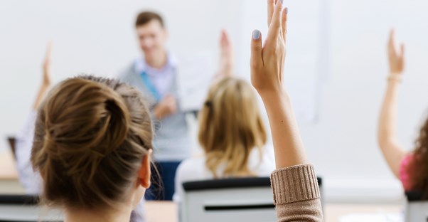Students raise their hands after a teacher asks a question