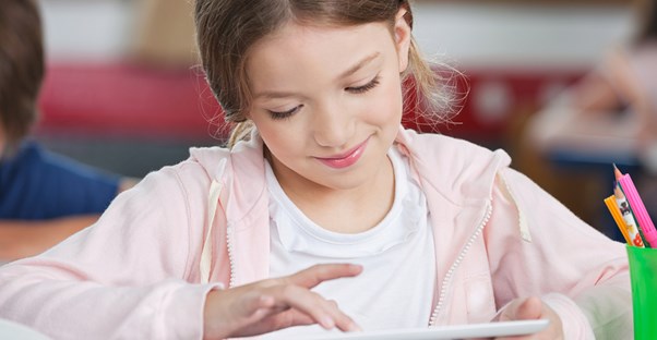 a young girl plays with her tablet at school