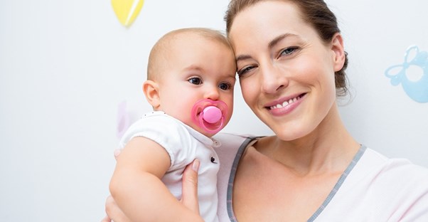 A breastfeeding mother smiles while holding her pacifier loving baby