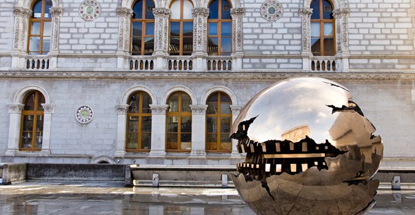 Giant metallic sphere shaped sculpture sits next to an old building