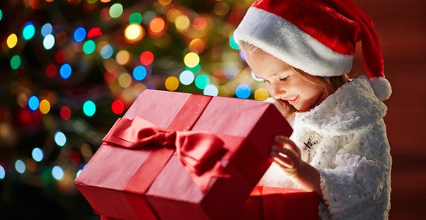 A young girl opens a Christmas gift and the light from the box shines on her face.