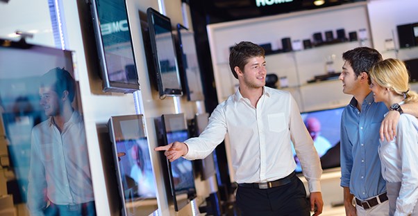 A sales associate shows off a display TV to a prospective couple.