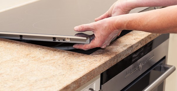 A homeowner reinstalling a stovetop after fixing a damaged countertop