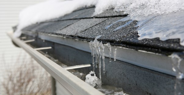 A close up of a shingled roof covered in snow and ice