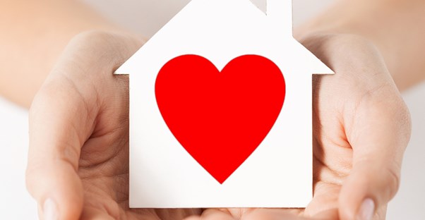 Hands holding a paper house with a heart in it to represent that donating is good for you.