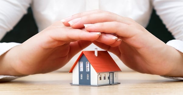 Hands covering a house representing protection of umbrella insurance
