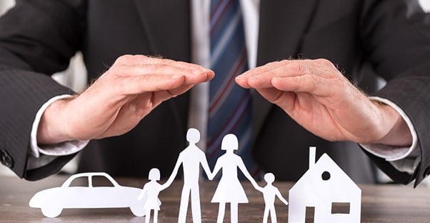 a paper cut out of a family with two kids and a house and a car standing up on a table with the hands of a man in a suit covering them like term life insurance covers families
