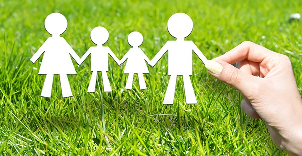 a paper cut out of a family with two kids being held by a womans hand over some very green grass to show that life with the right term life insurance policies is always better for your family 