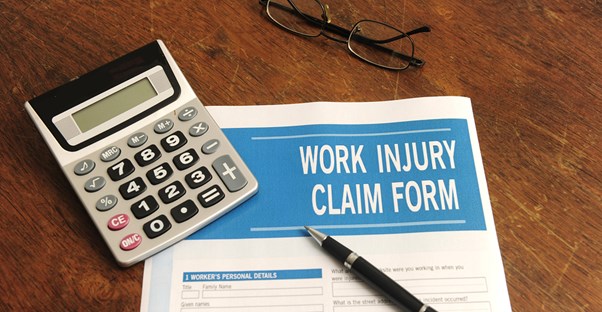 A work injury claim form, calculator, pen, and glasses sitting on a desk