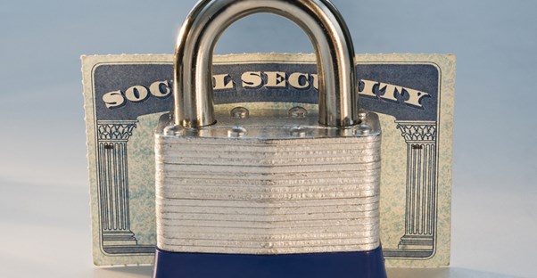 A lock standing in front of a social security card to represent the advantages and disadvantages of social security.