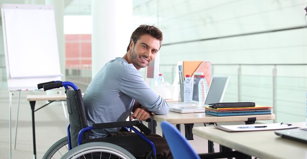 Man in a wheelchair smiling while using his laptop