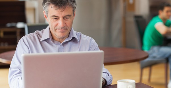 man researching IRA loans on a laptop with a cup of coffee.