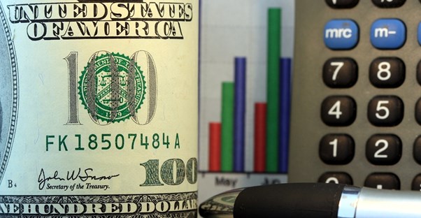 One hundred dollar bill next to the corner of a calculator and small bar graph of company assets