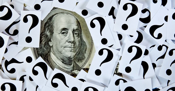 Ben Franklin on a bill surrounded by question marks on paper