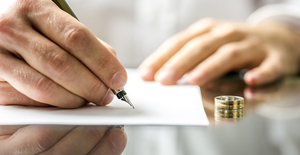 Man signing divorce papers with his ring on his desk