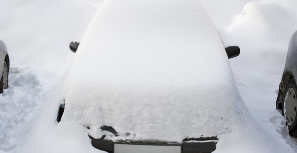 A car covered in snow because it doesn't have a car cover