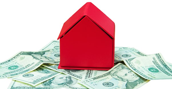A toy red house sitting on top of a pile of twenty dollar bills on a white surface and background to show that escrow companies take care of your money