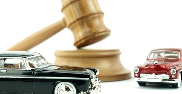 a light wood gavel resting on a sounding block with a toy red antique town car on the right side and a black version of the same toy car in front of it to show that you can bid on cars at auctions