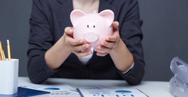 a woman behind a desk of financial information holds a piggy bank