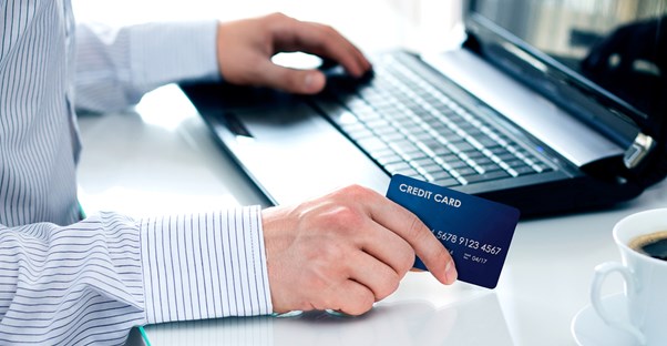 Man holding credit card as he searches for the top credit card processing companies on his computer.