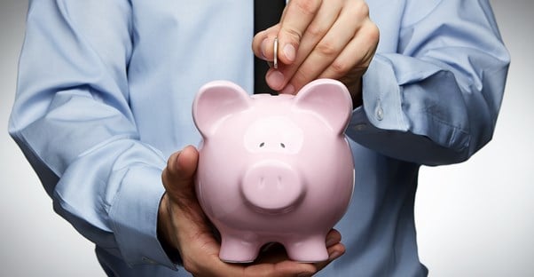 Man placing money in a piggy bank to represent how guarantor loans can cost you a lot of money.