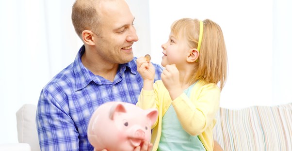 Man uses a piggy bank to explain saving money and budgeting to his young daughter.