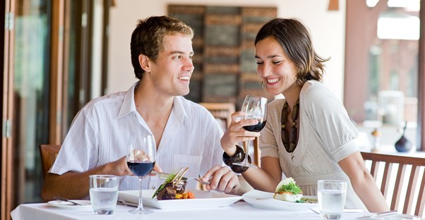 A young couple smiles while they eat dinner because they saved money with coupons and specials.