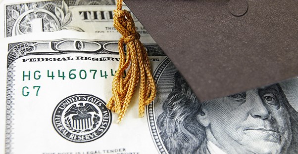 A college graduation cap resting on a hundred dollar bill obtained through financial aid.
