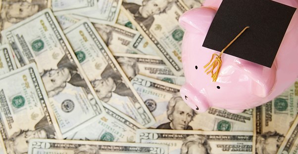 A pink piggy bank where a graduation cap sitting on top of money gained from a college loan.
