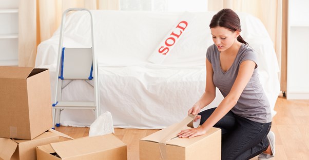 Woman Unpacking Boxes Next to Sold Sign