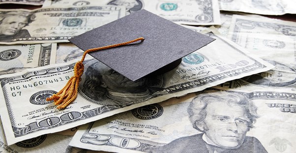 Tiny graduation cap on top of a pile of student loan cash
