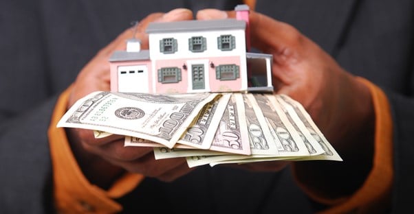 Man holding a house and cash from a low interest home equity loan